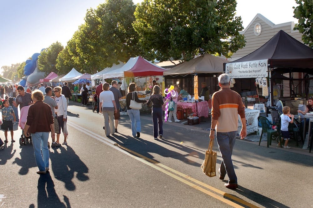 Shoppers walking a covered aisle of produce stands at a San Diego farmers market